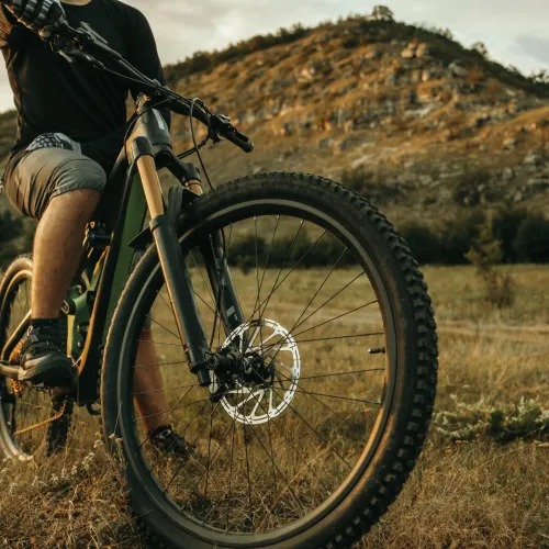 Mies ajaa maastopy&ouml;r&auml;ll&auml; luonnossa, taustalla kukkula ja pilvinen taivas.