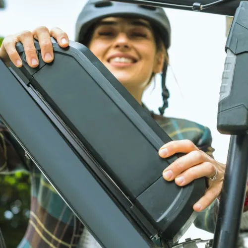 Nainen asettaa akun s&auml;hk&ouml;py&ouml;r&auml;&auml;n, hymyillen.