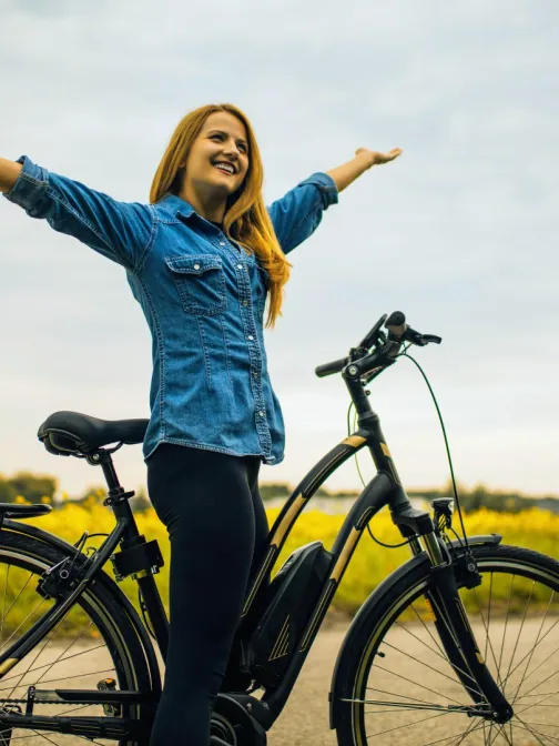 Nainen seisoo py&ouml;r&auml;n vieress&auml; pellon laidalla, k&auml;det ylh&auml;&auml;ll&auml; iloisena.