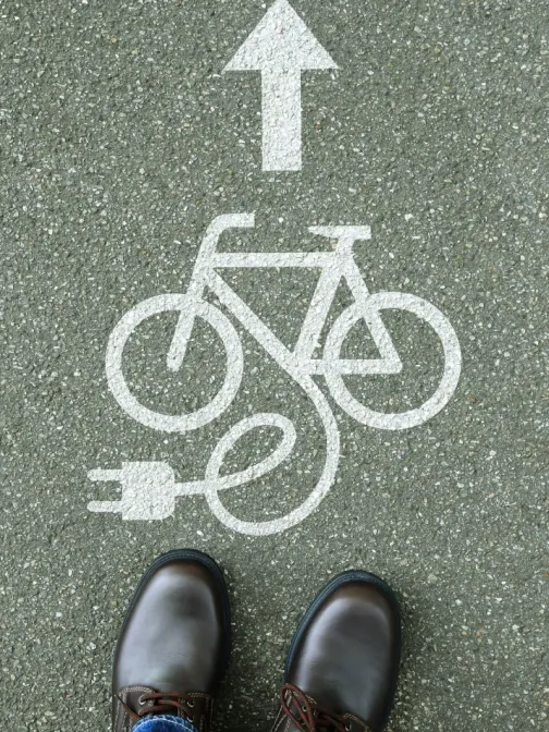 S&auml;hk&ouml;py&ouml;r&auml;tiekuvake asfaltilla, nuoli yl&ouml;sp&auml;in, edess&auml; ruskeat keng&auml;t.