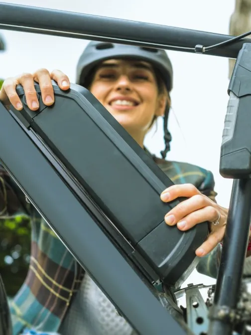 Nainen asettaa akun s&auml;hk&ouml;py&ouml;r&auml;&auml;n, hymyillen.