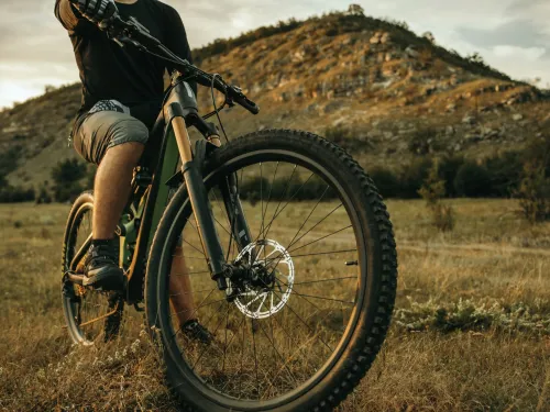 Mies ajaa maastopy&ouml;r&auml;ll&auml; luonnossa, taustalla kukkula ja pilvinen taivas.